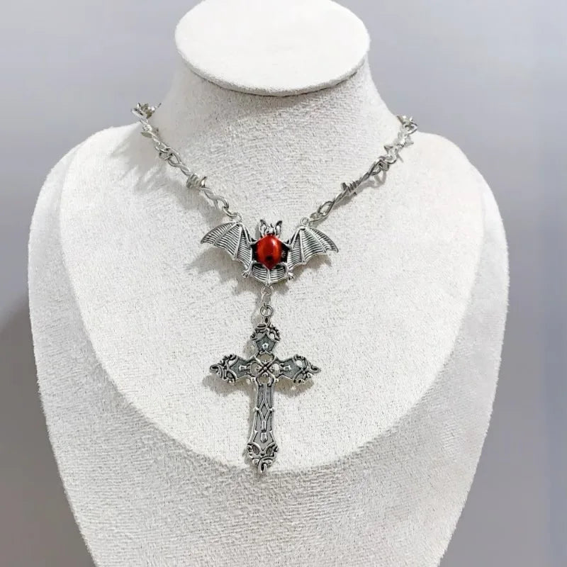 Collar gótico metálico con cuatro variantes: corazón, murciélago con ataúd, murciélago con cruz, joyería dark.
Esta imagen muestra la variante de murcielago con cruz y alambre.
