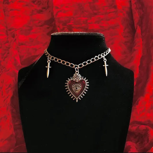 Collar gótico metálico con cuatro variantes: corazón, murciélago con ataúd, murciélago con cruz, joyería dark.
Esta imagen muestra la variante con corazón.