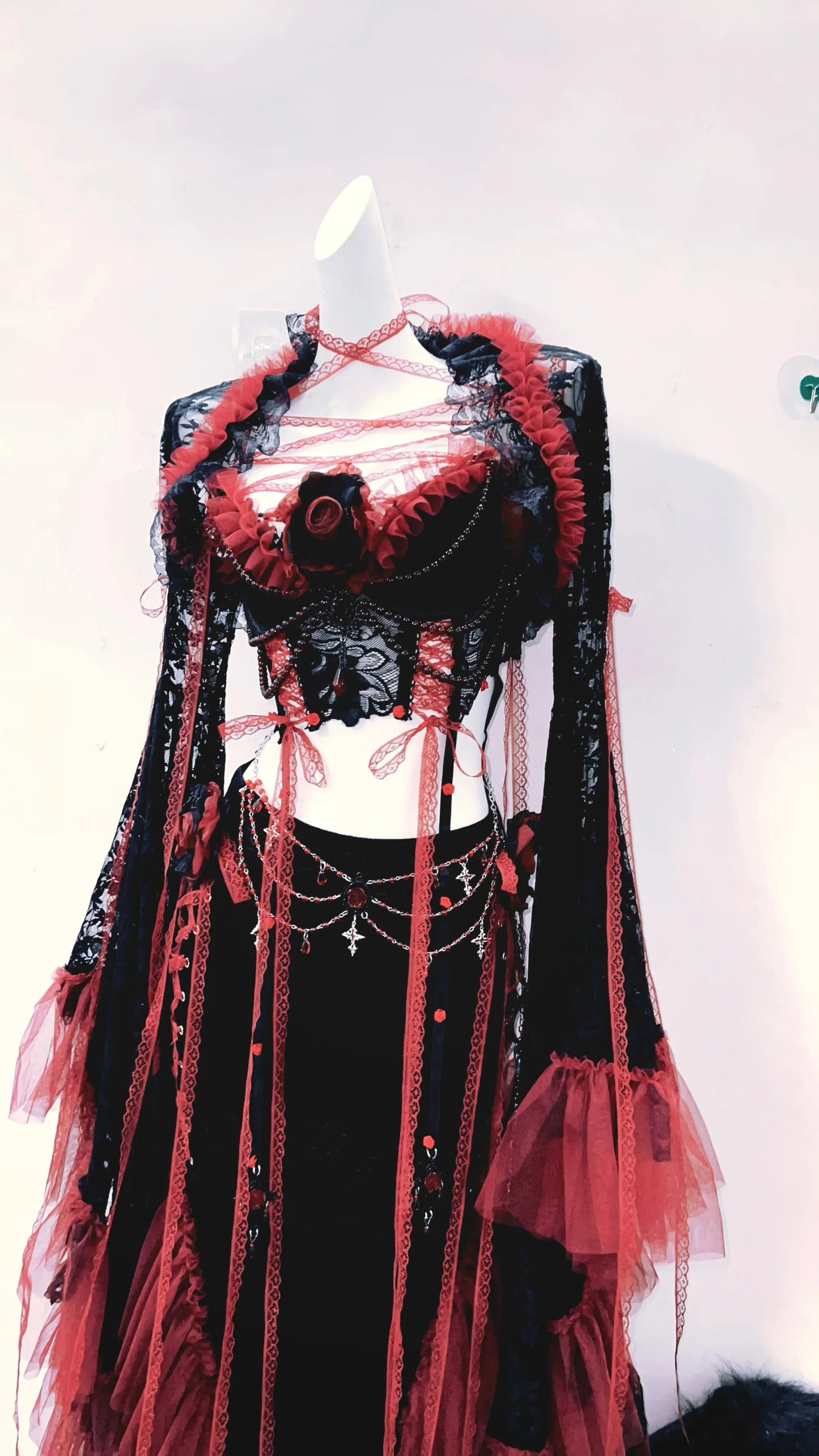 lateral derecho de un conjuto vestido completo separado, con top corto, mangas largas y falda larga, de colores rojo y negro con tiras rojas de tela