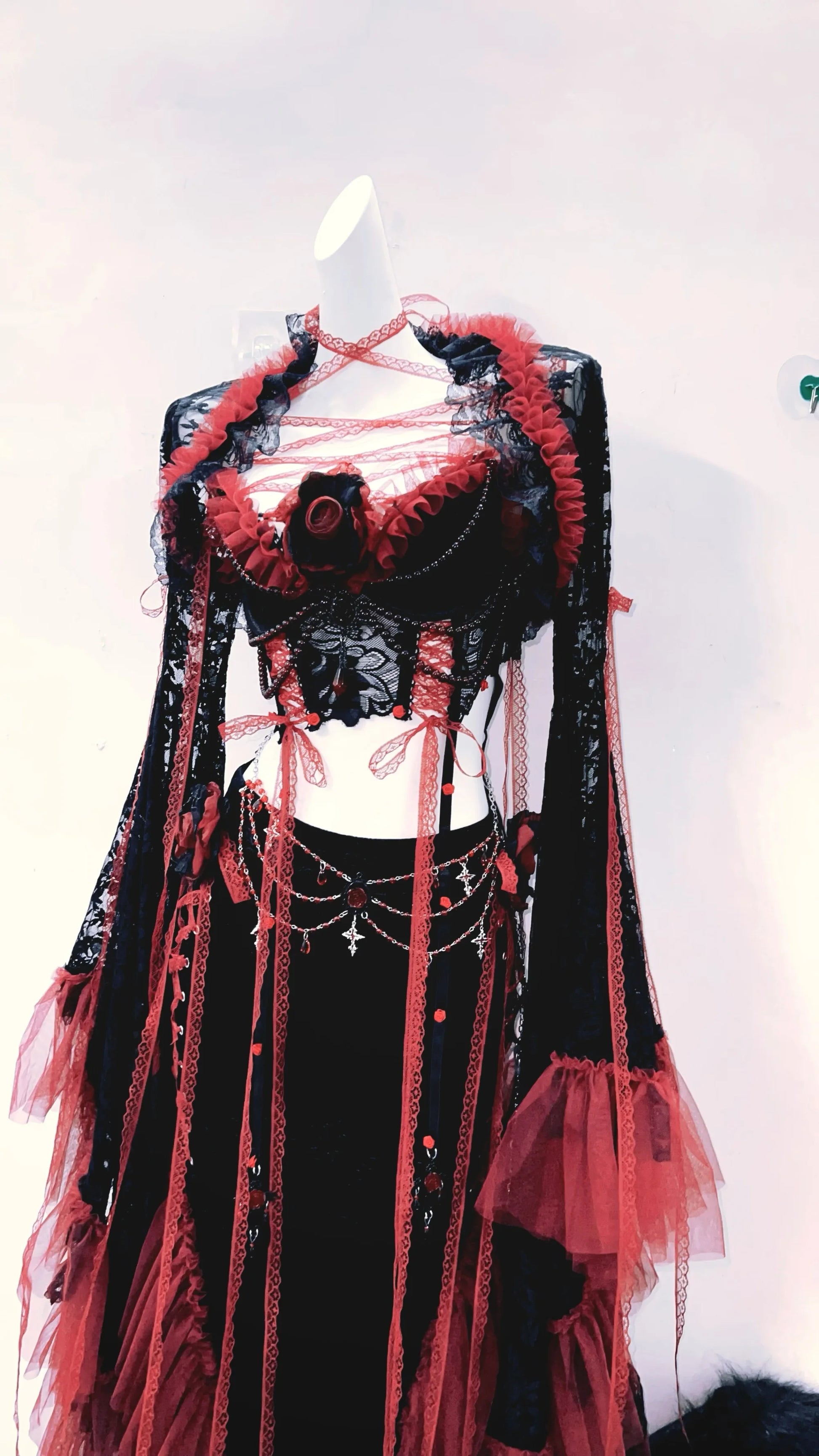 lateral derecho de un conjuto vestido completo separado, con top corto, mangas largas y falda larga, de colores rojo y negro con tiras rojas de tela