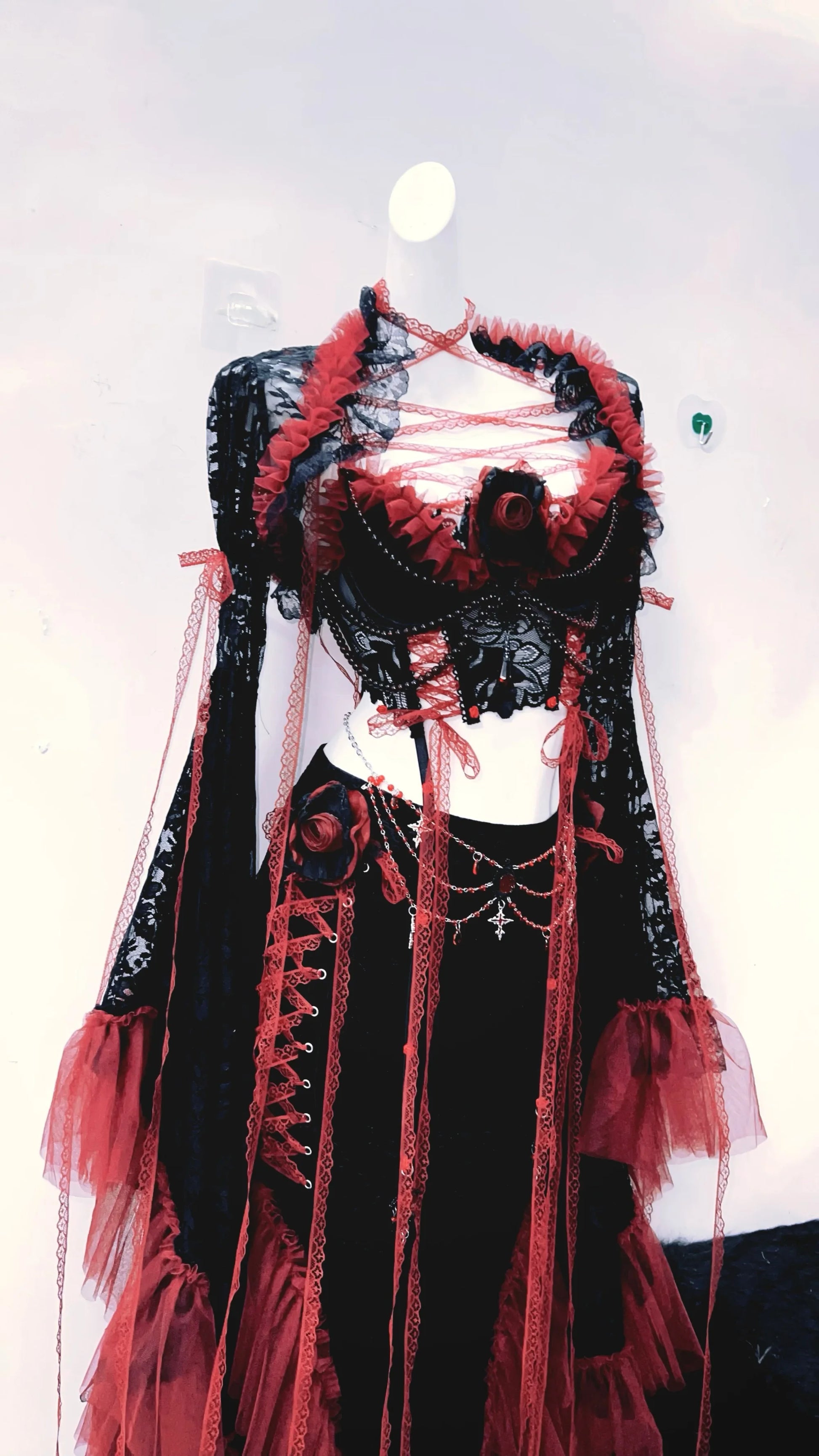 lateral izquierdo de un conjuto vestido completo separado, con top corto, mangas largas y falda larga, de colores rojo y negro con tiras rojas de tela