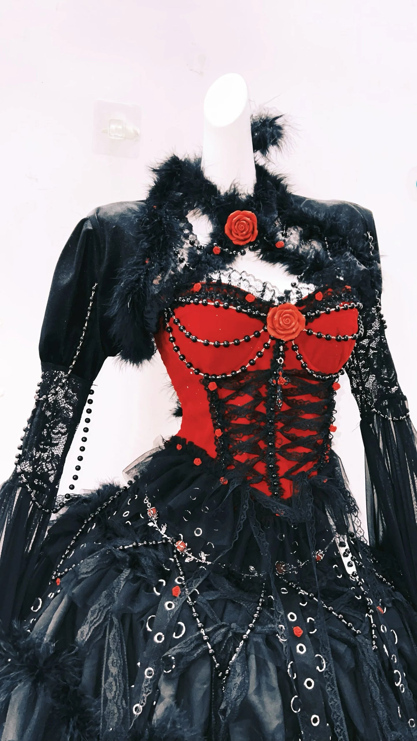 Parte superior mostrada de lado, vestido gotico rojo y negro con pelaje y detalles metalicos. Tiene una flor en el cuello y escote